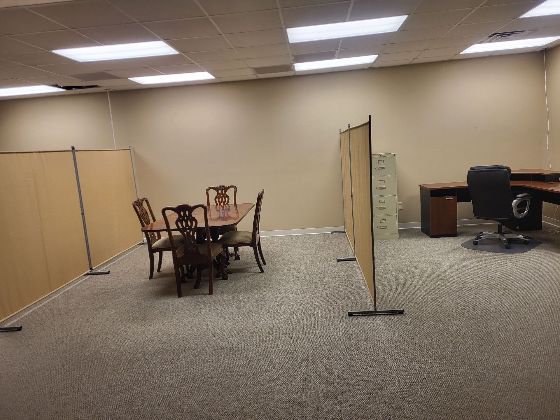 Office space with a table, chairs, desks, and partitions. Beige walls and carpet.