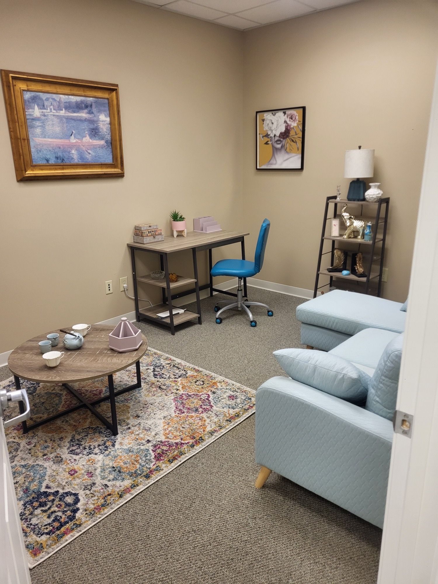 Cozy office: desk, blue chair, loveseat, and coffee table with a patterned rug. Wall art and decor complete the space.