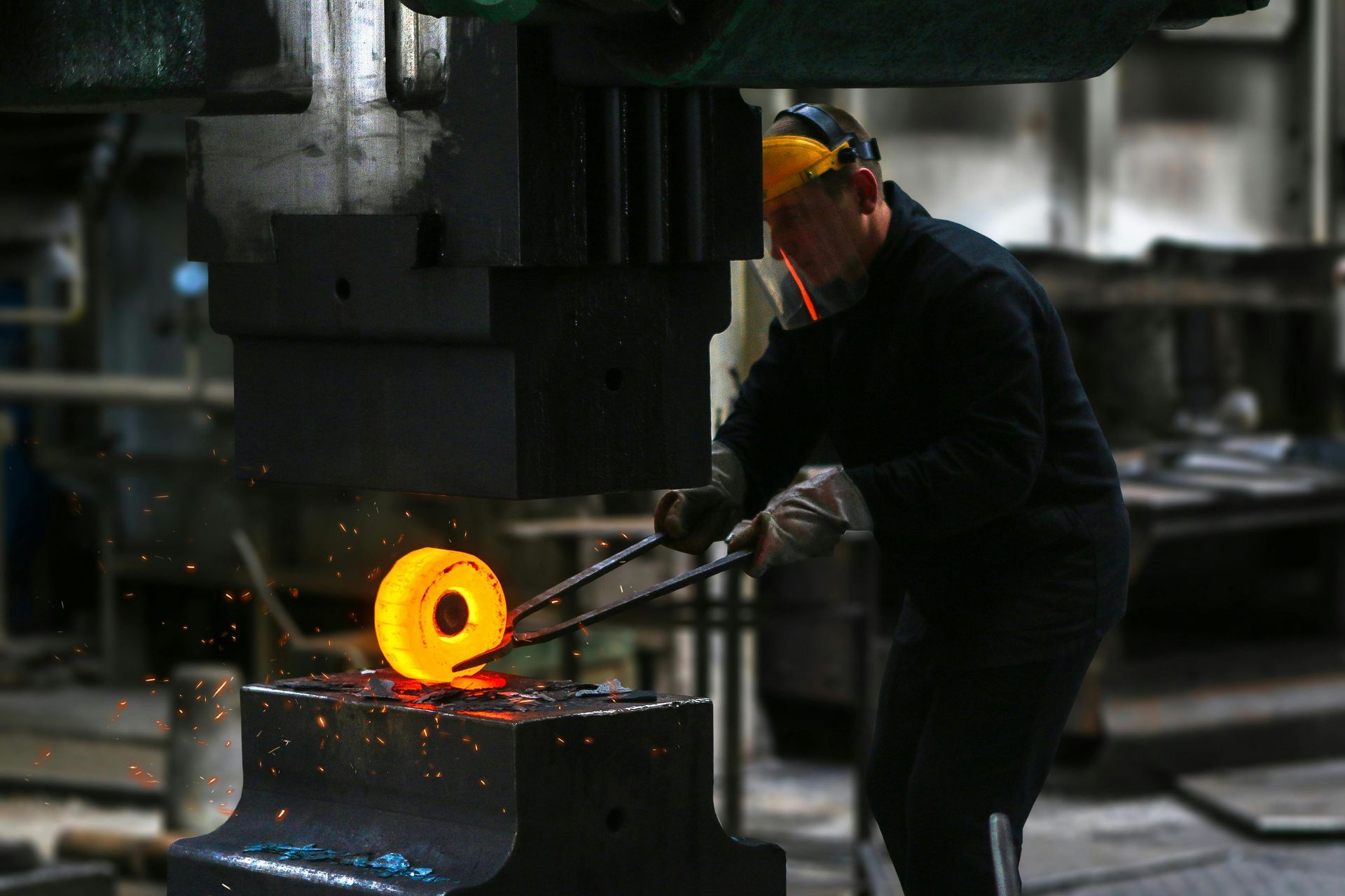 En man arbetar på en metallbit med en maskin i en fabrik.
