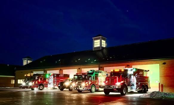 Fire trucks with Christmas decorations parked in front of a fire station at night.