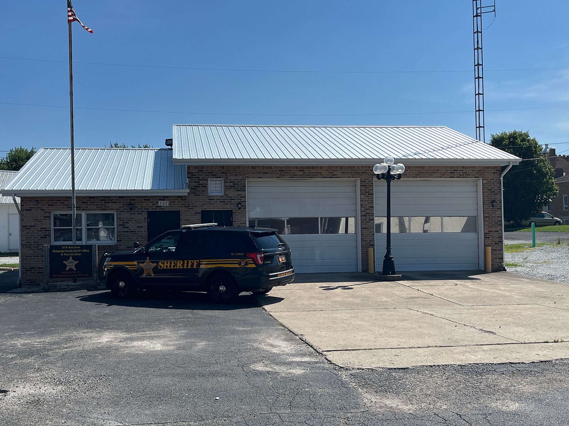 Sheriff's office building with a black SUV parked out front. Two garage doors and a flagpole visible.