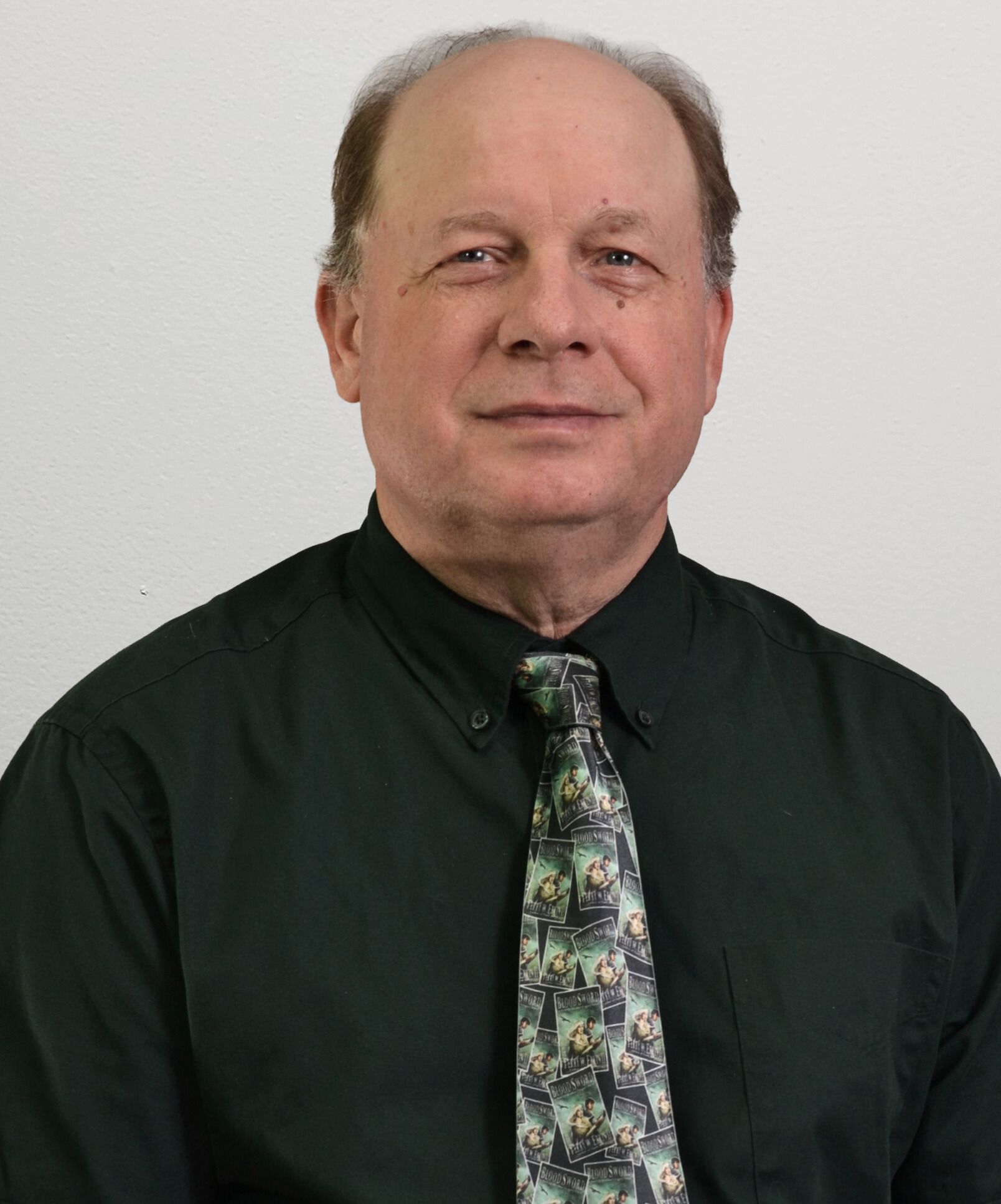 Man in green shirt and patterned tie against a plain background.