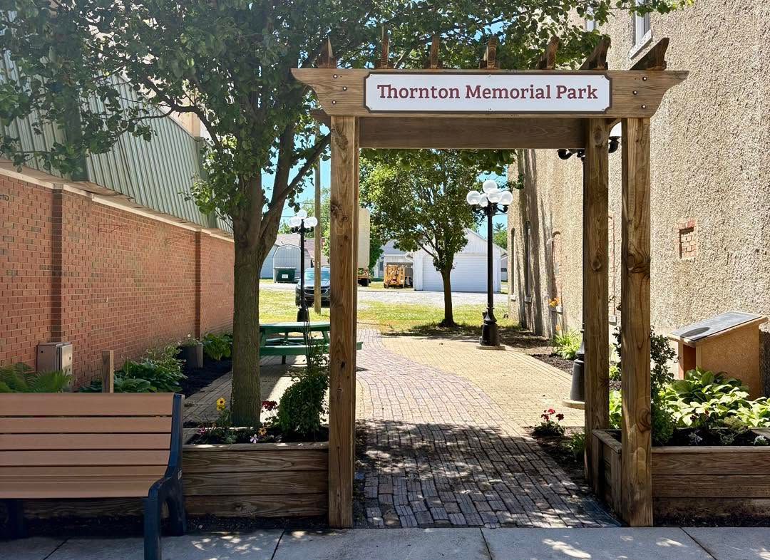 Entrance to Thornton Memorial Park with a wooden archway, brick path, benches, and trees