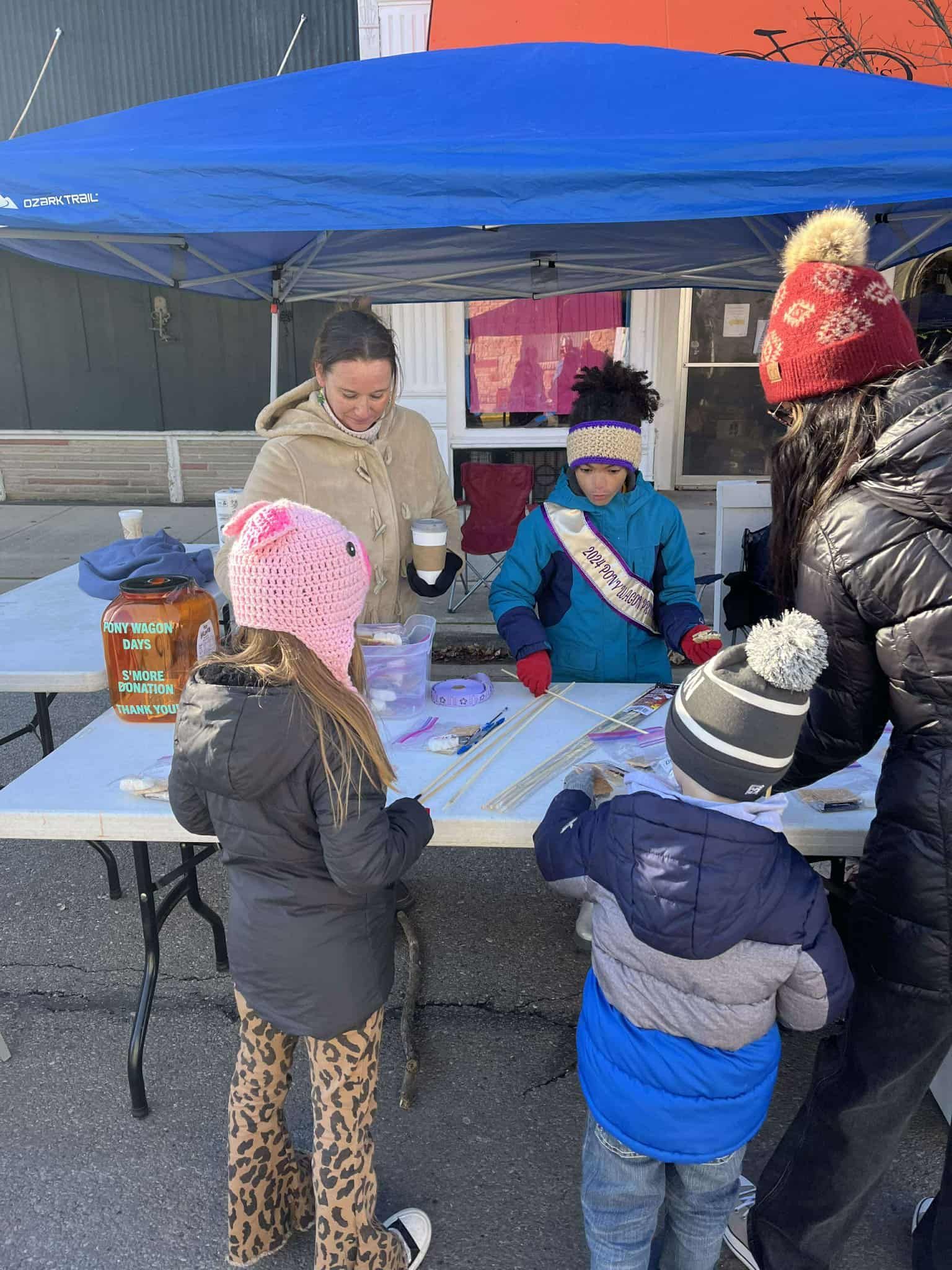 People at a table under a blue canopy. Children are shopping, and an adult is attending the table.