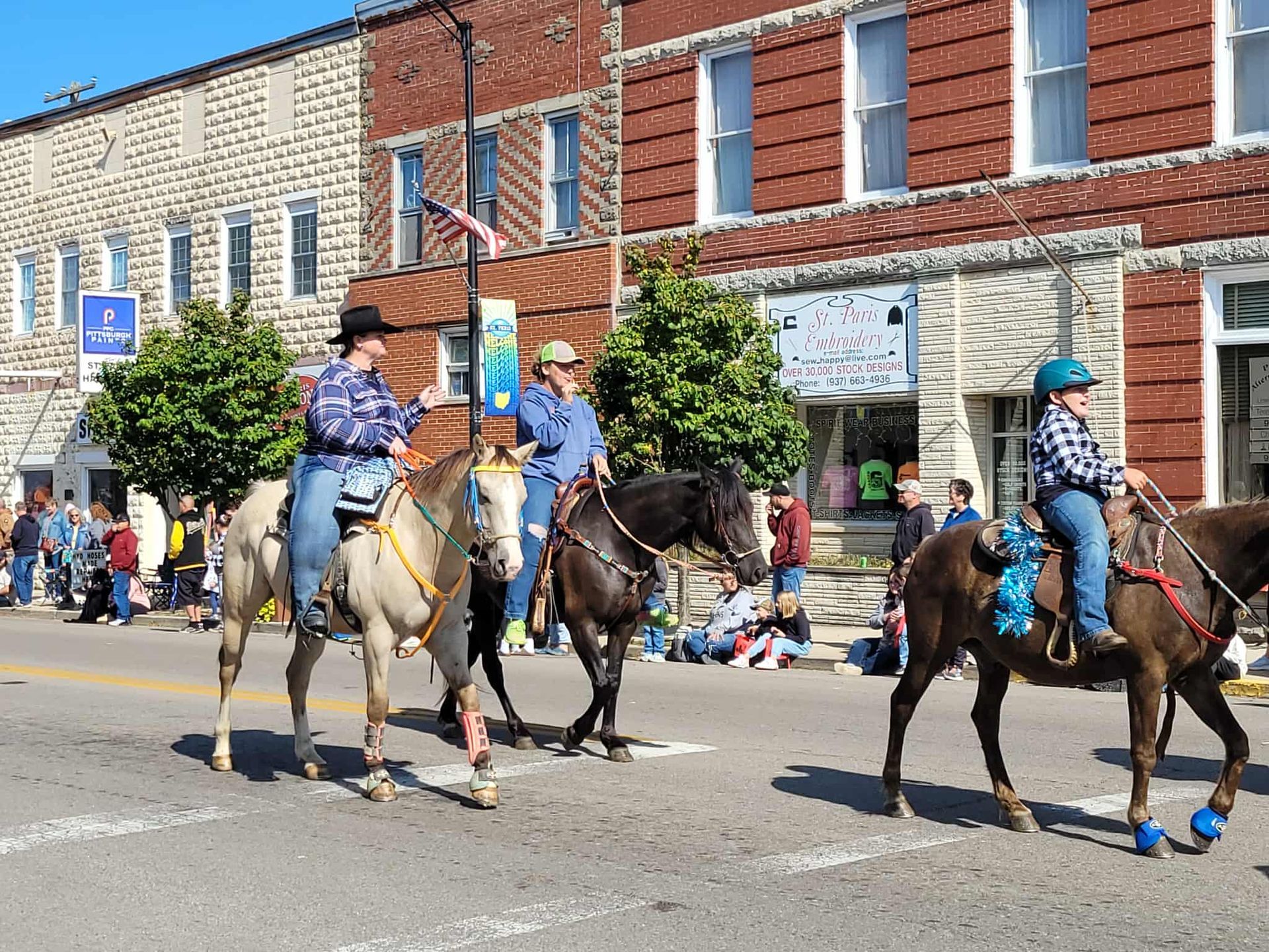 Three people on horseback in a parade, riding down a street lined with buildings and onlookers.