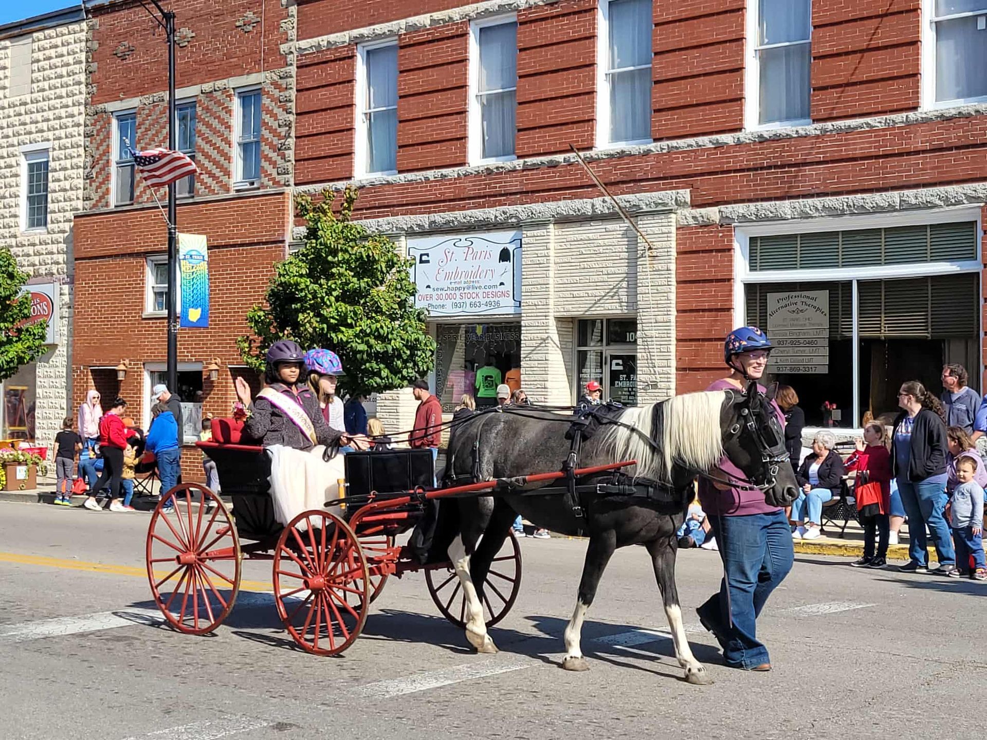 Horse-drawn carriage in a parade on a street with brick buildings and spectators.