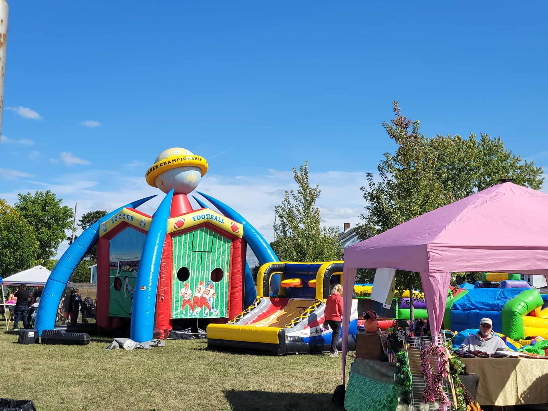 Inflatable play structure at outdoor event with pink tent and blue sky.