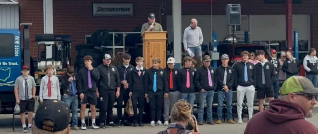 People stand in front of a building. A speaker at a podium. People wearing black jackets, colored ties.