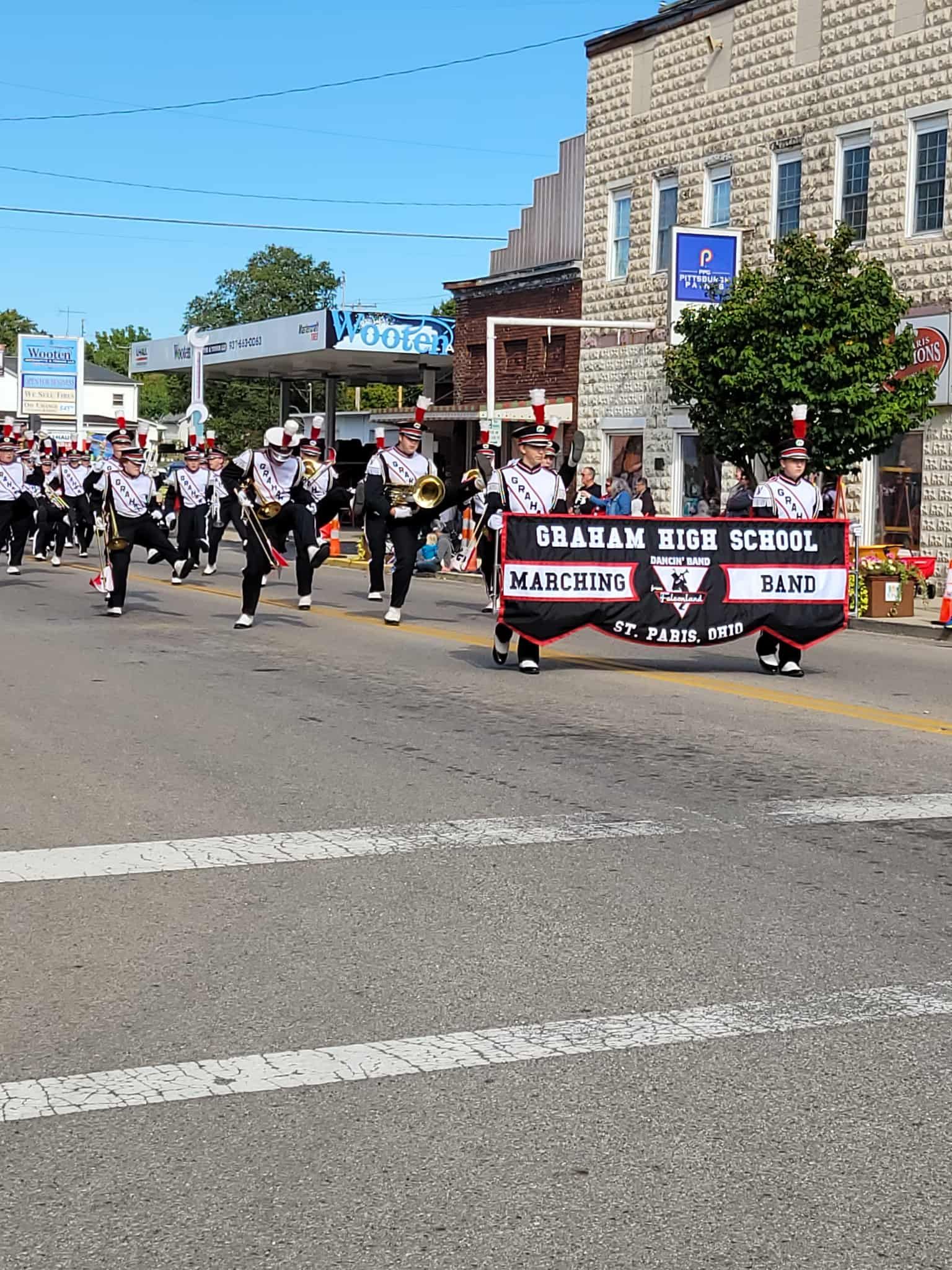 Marching band parades down street, carrying banner that reads