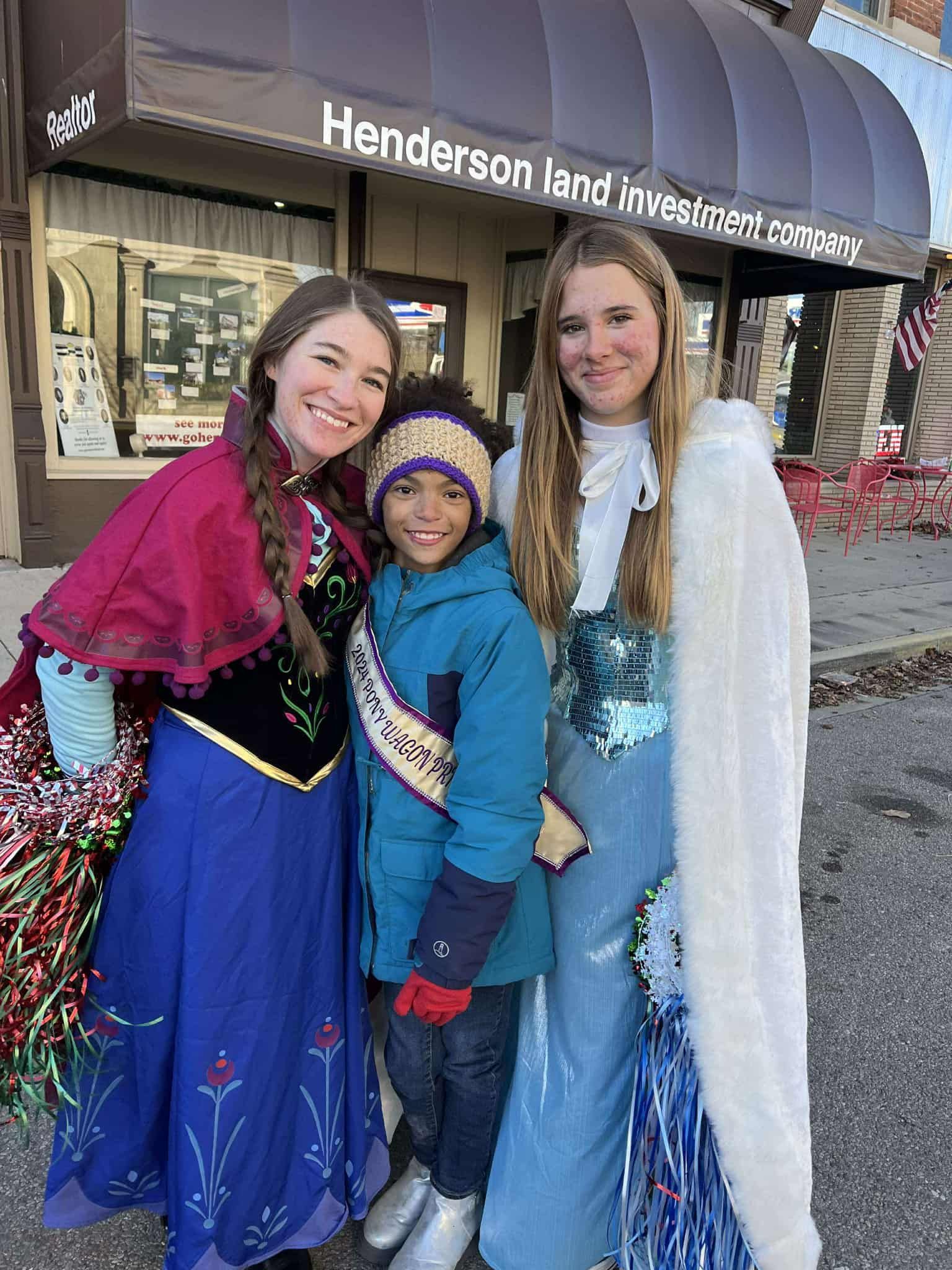 Two women in princess costumes pose with a child in front of a store.
