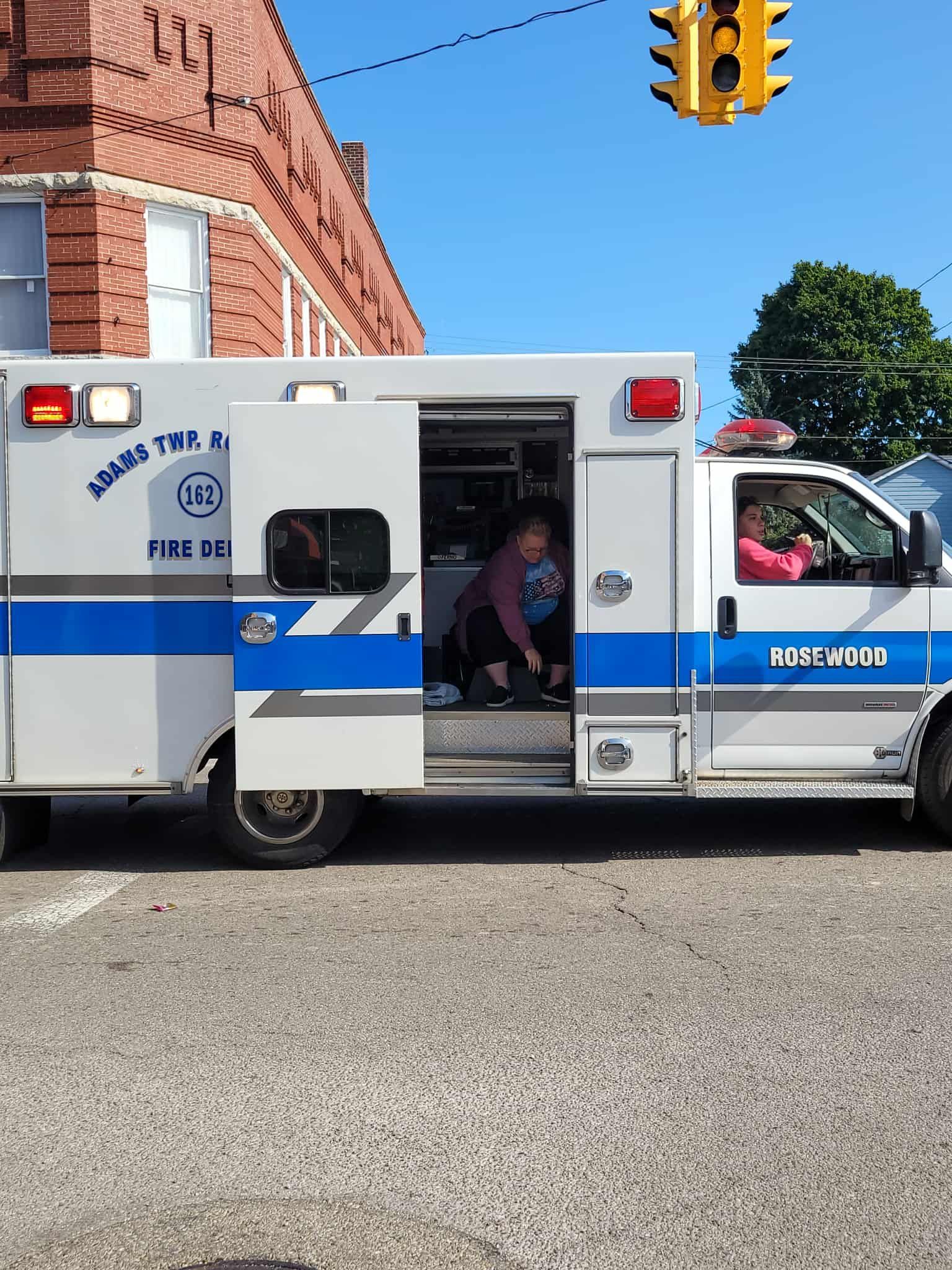 Ambulance with open door, people inside; parked on a street near a brick building and traffic light.