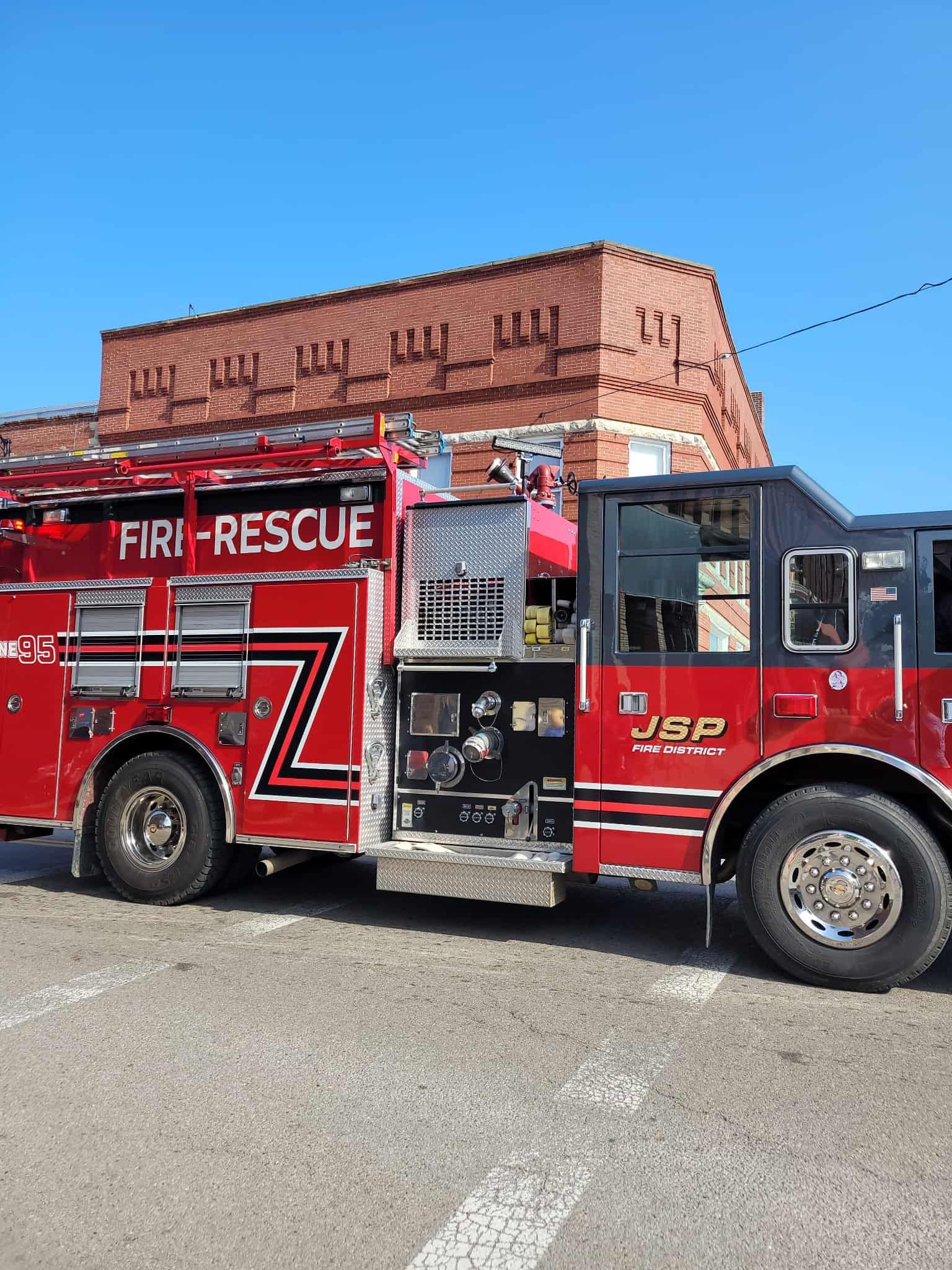Red fire truck parked in front of a brick building on a sunny day.