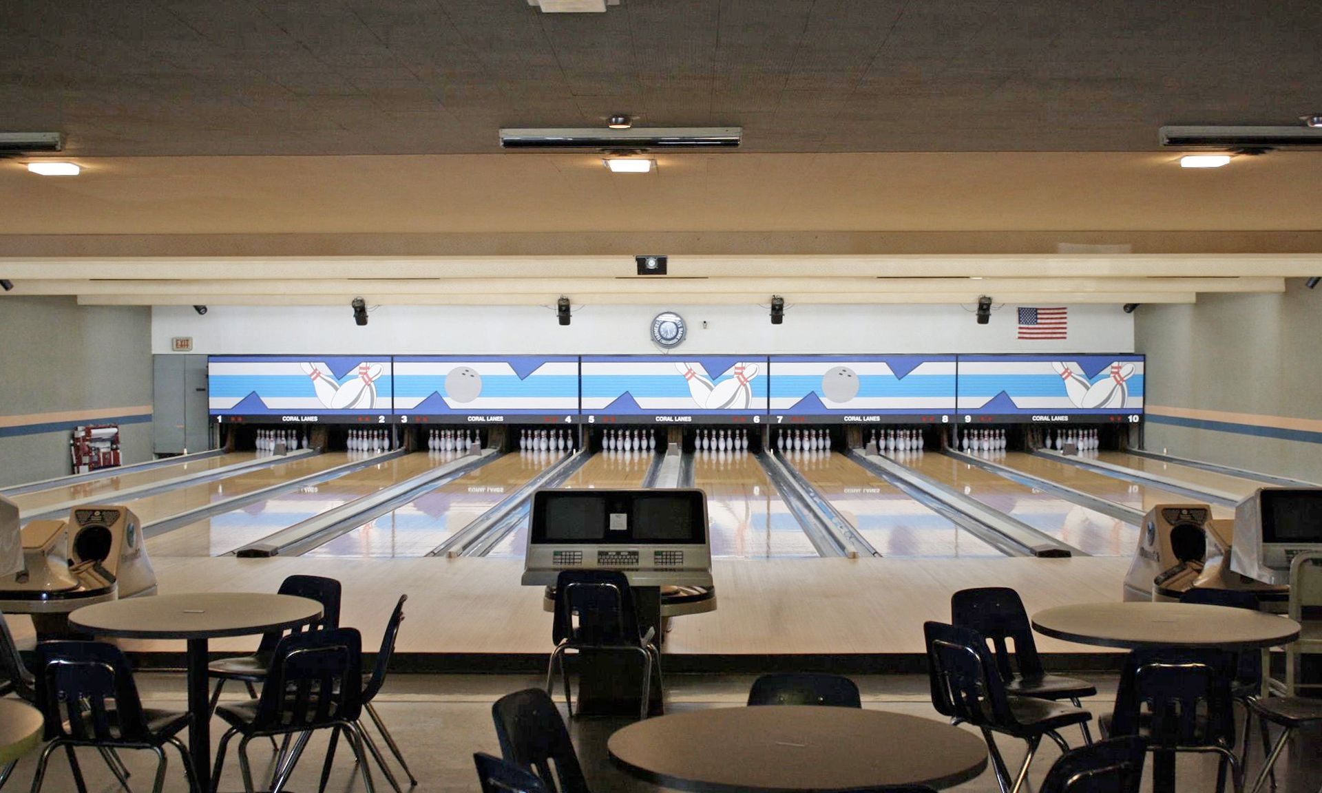 Bowling alley with lanes, pins, and round tables with chairs.