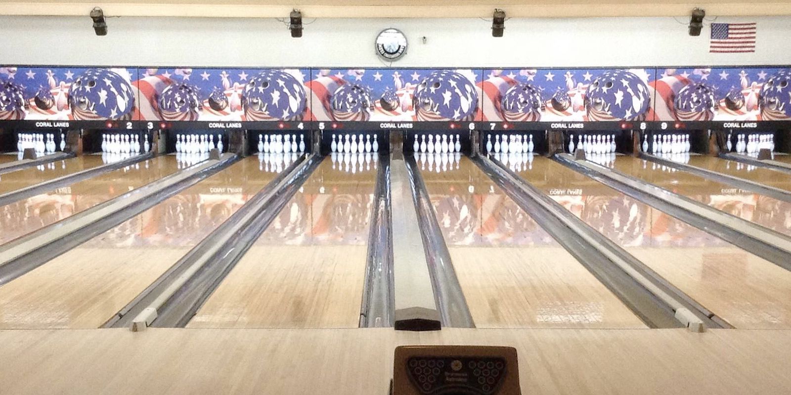 Bowling alley with multiple lanes and pins set up, patriotic decor and an American flag.
