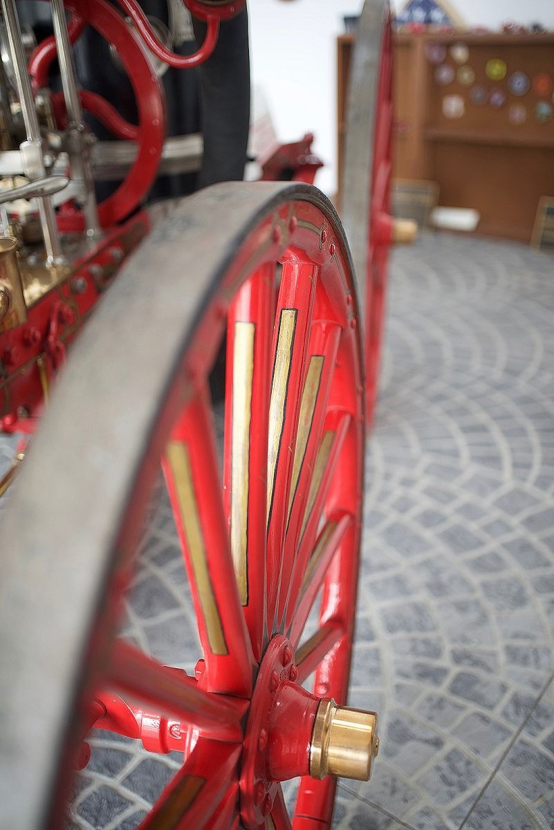 Red spoked wheel with brass accents on a vintage vehicle.
