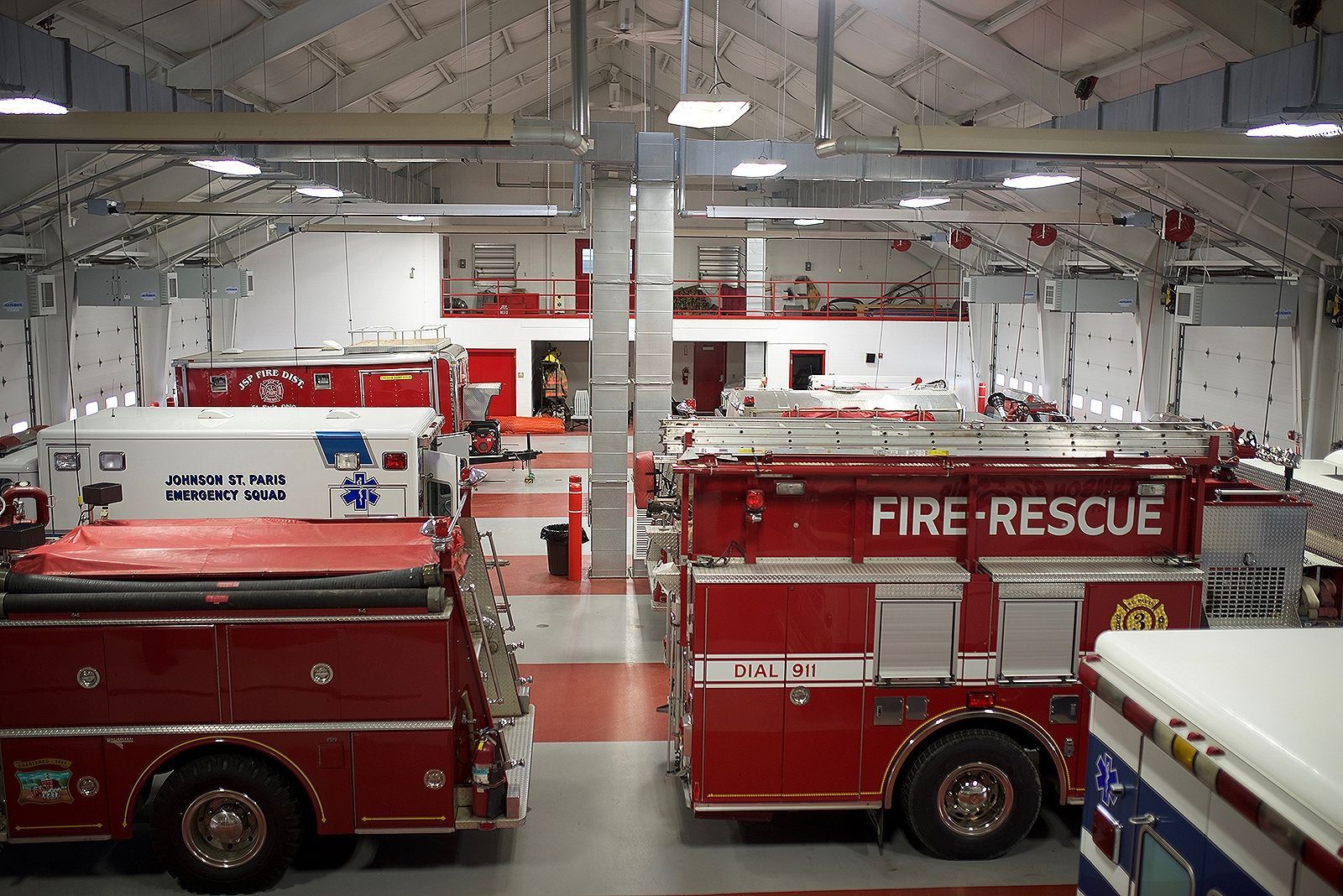 Fire station interior with red fire trucks parked inside; a fireman can be seen on the second story.
