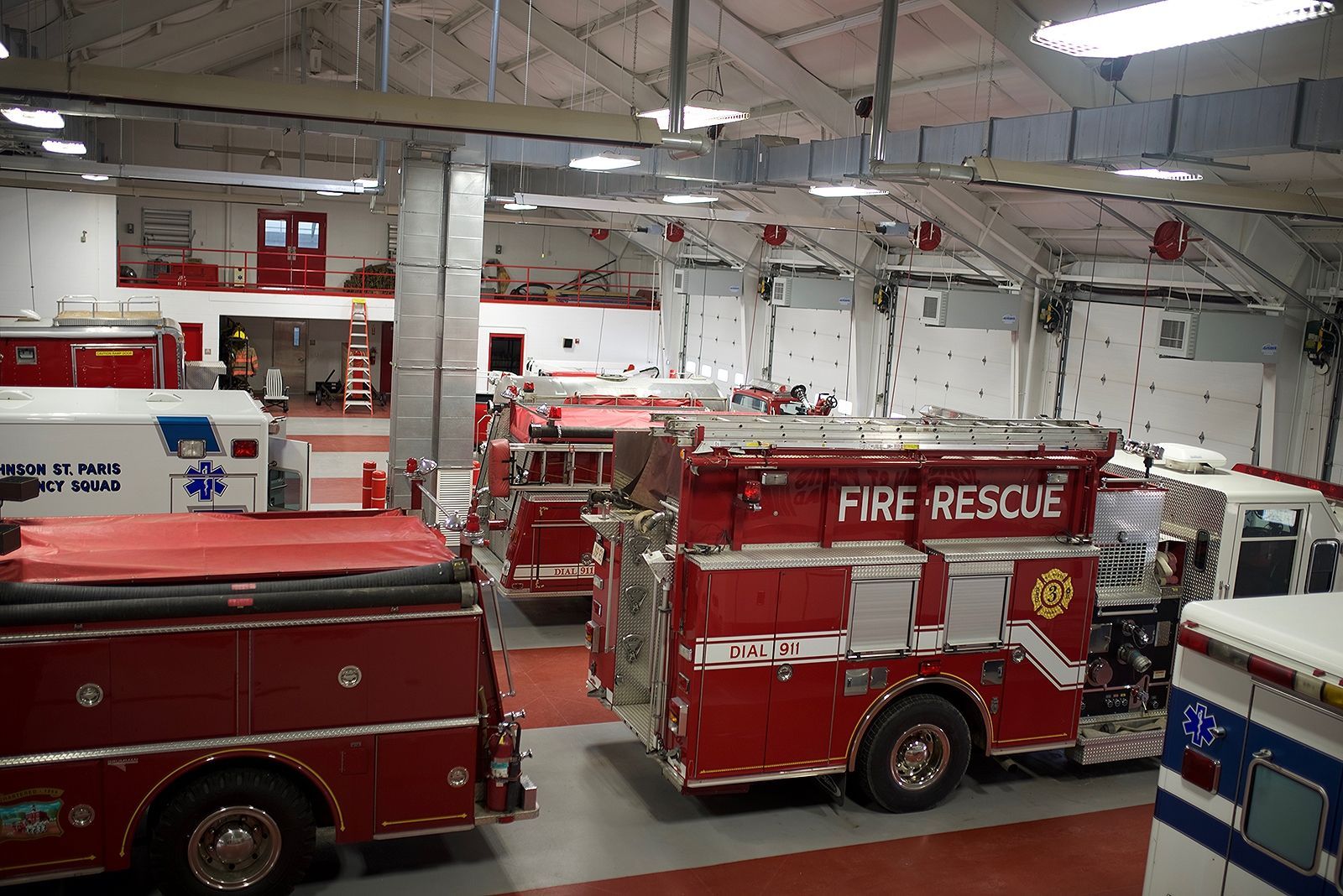 Fire station interior with multiple red fire trucks and an ambulance.