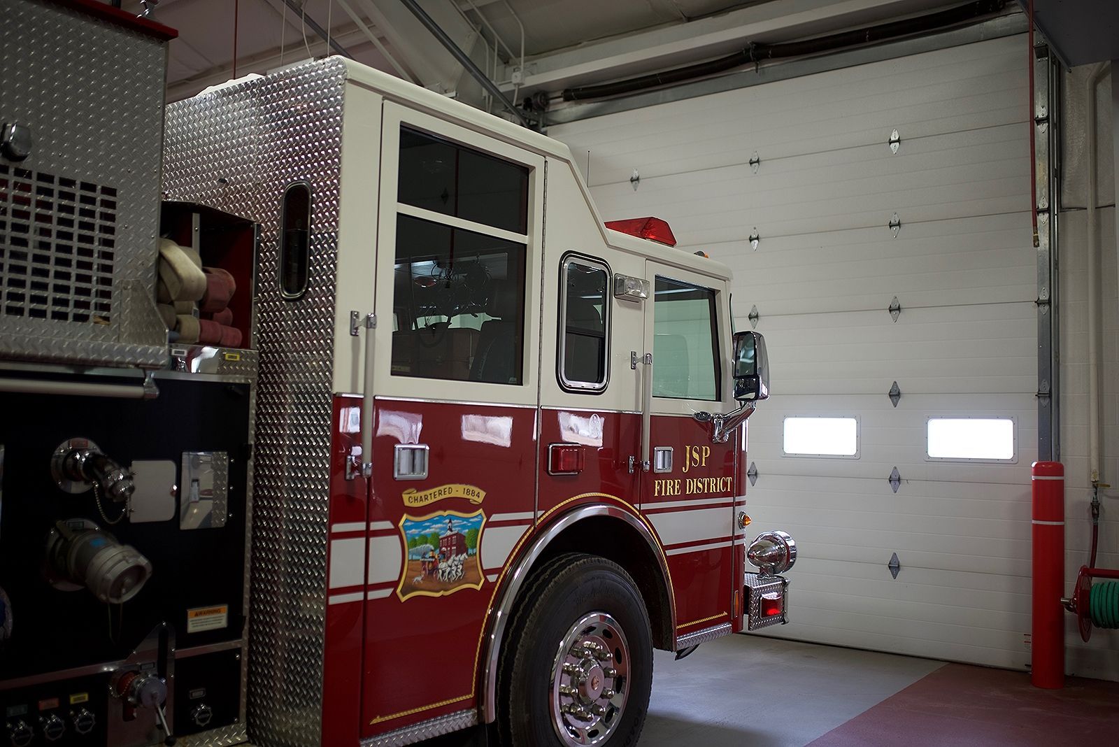 Fire truck inside a fire station bay with red, white, and silver coloring; garage door open.