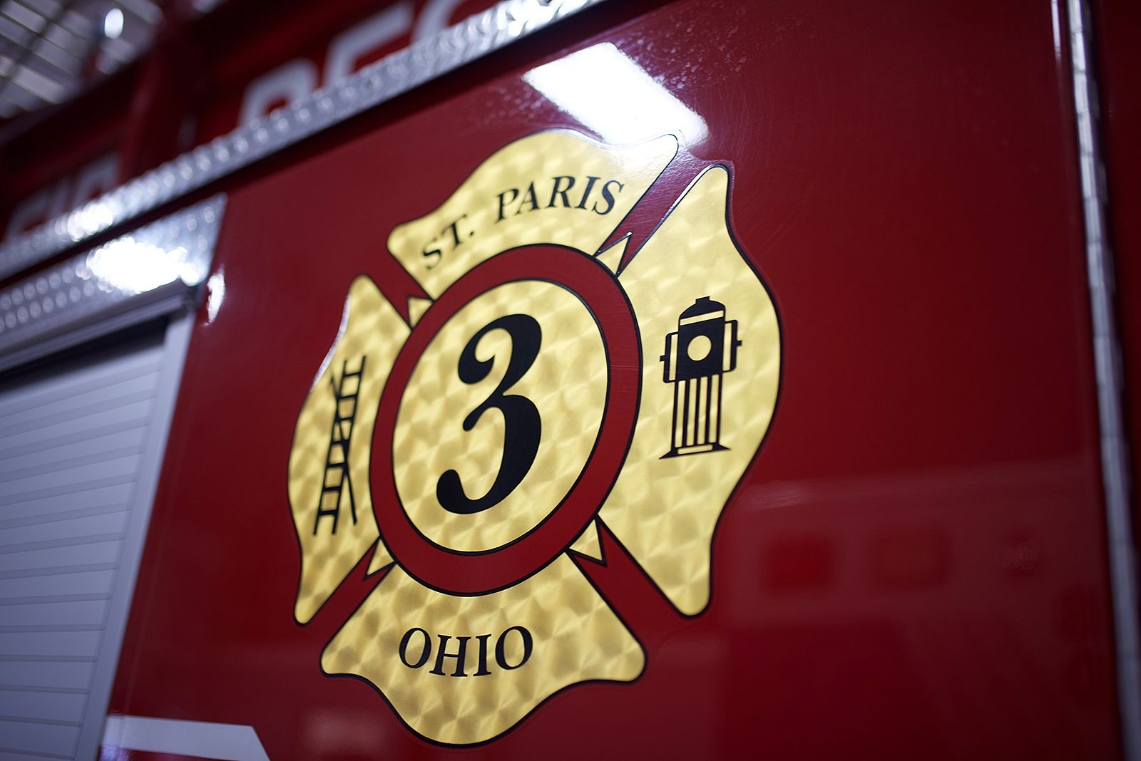 St. Paris, Ohio fire department emblem on red vehicle. Gold Maltese cross with a 3 and hydrant symbol.