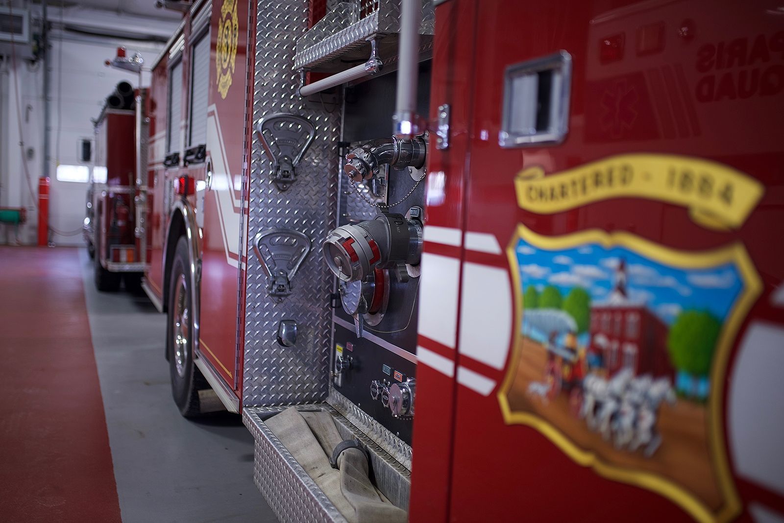 Red fire truck in a garage, showcasing the side with equipment and a town emblem.