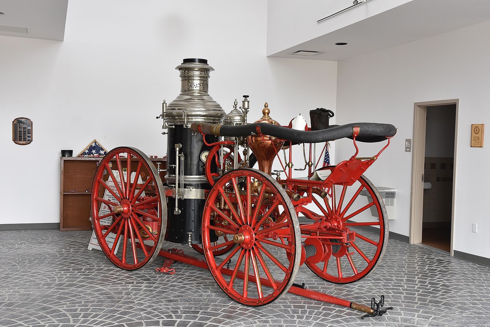 Antique fire engine with red wheels, displayed in a museum setting. Black and silver details.