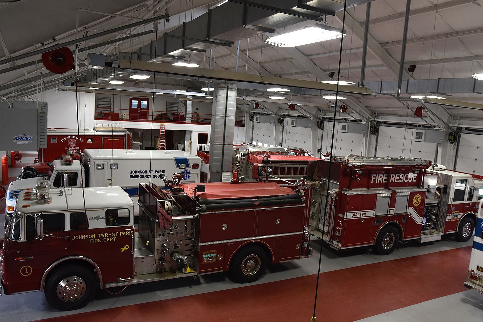 Fire station interior with red fire trucks and a white ambulance parked inside.