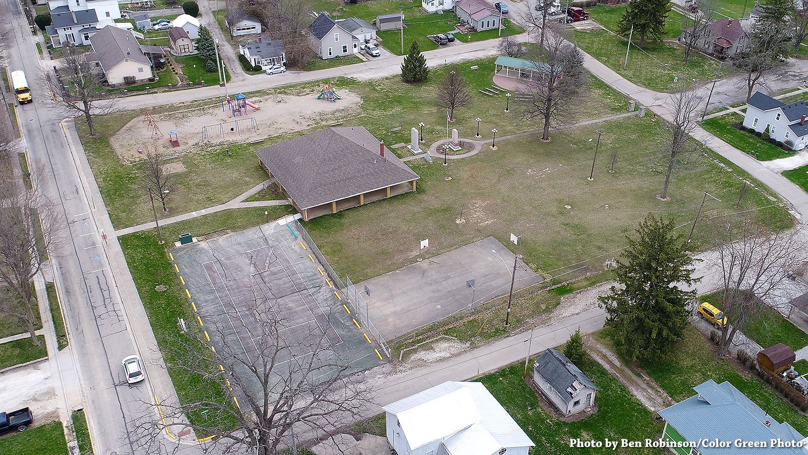 Aerial view of a park with a playground, building, and volleyball courts in a residential area.