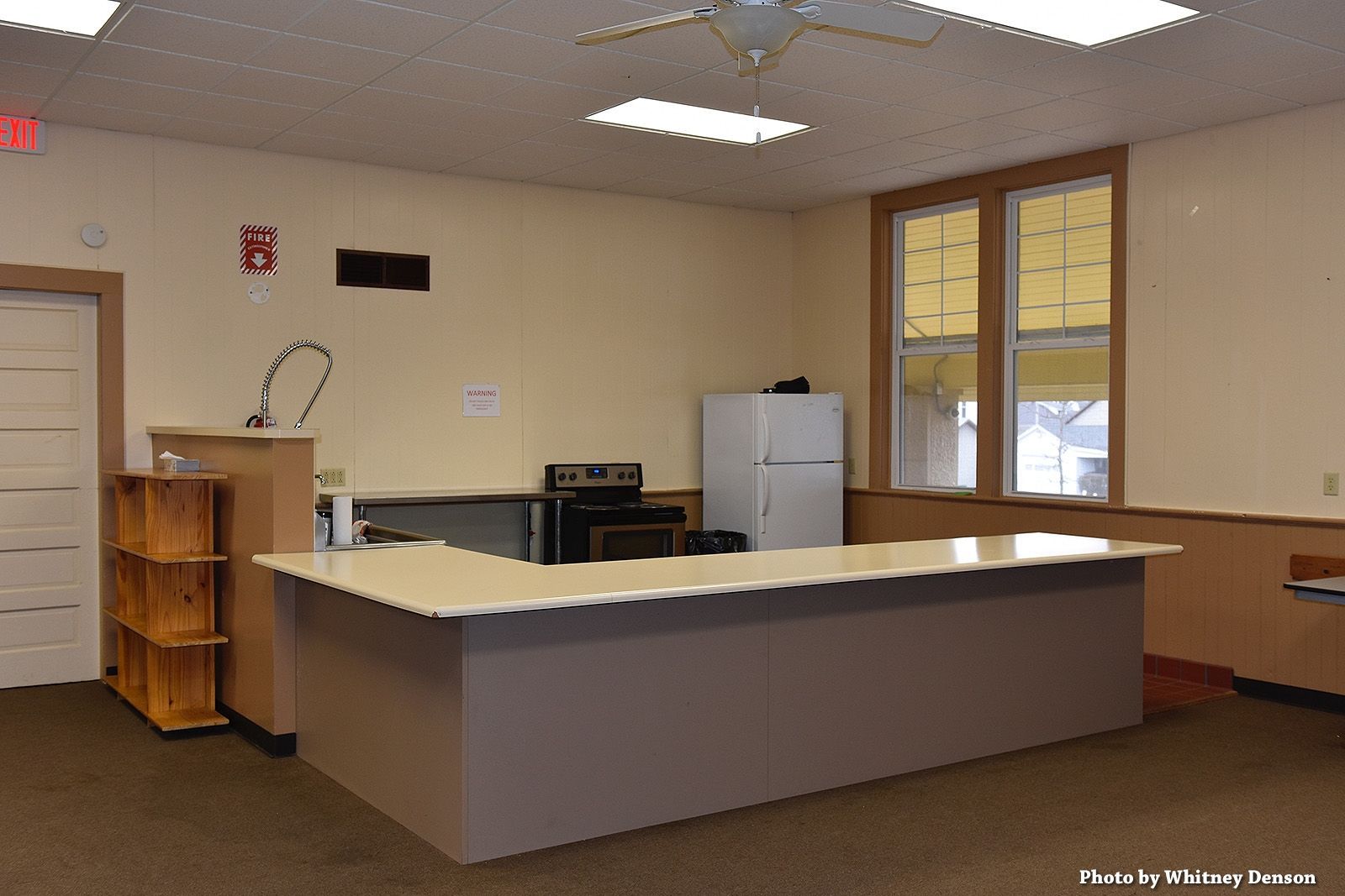 Interior view of a kitchen area with counter, stove, refrigerator, and window. Yellow walls.