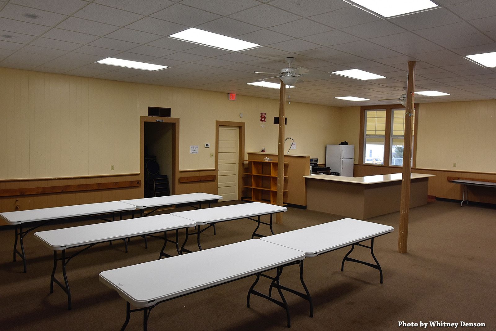 Empty room with long white tables, beige walls, and brown carpet.