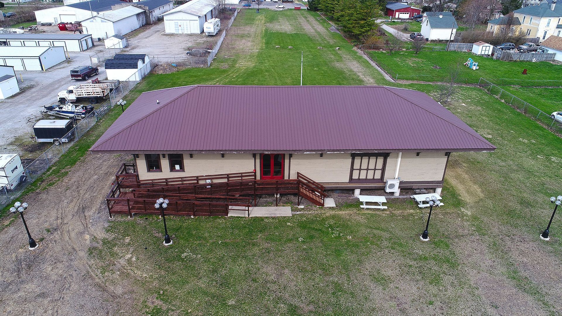 A brown building with a burgundy roof, possibly a train station, surrounded by green grass.
