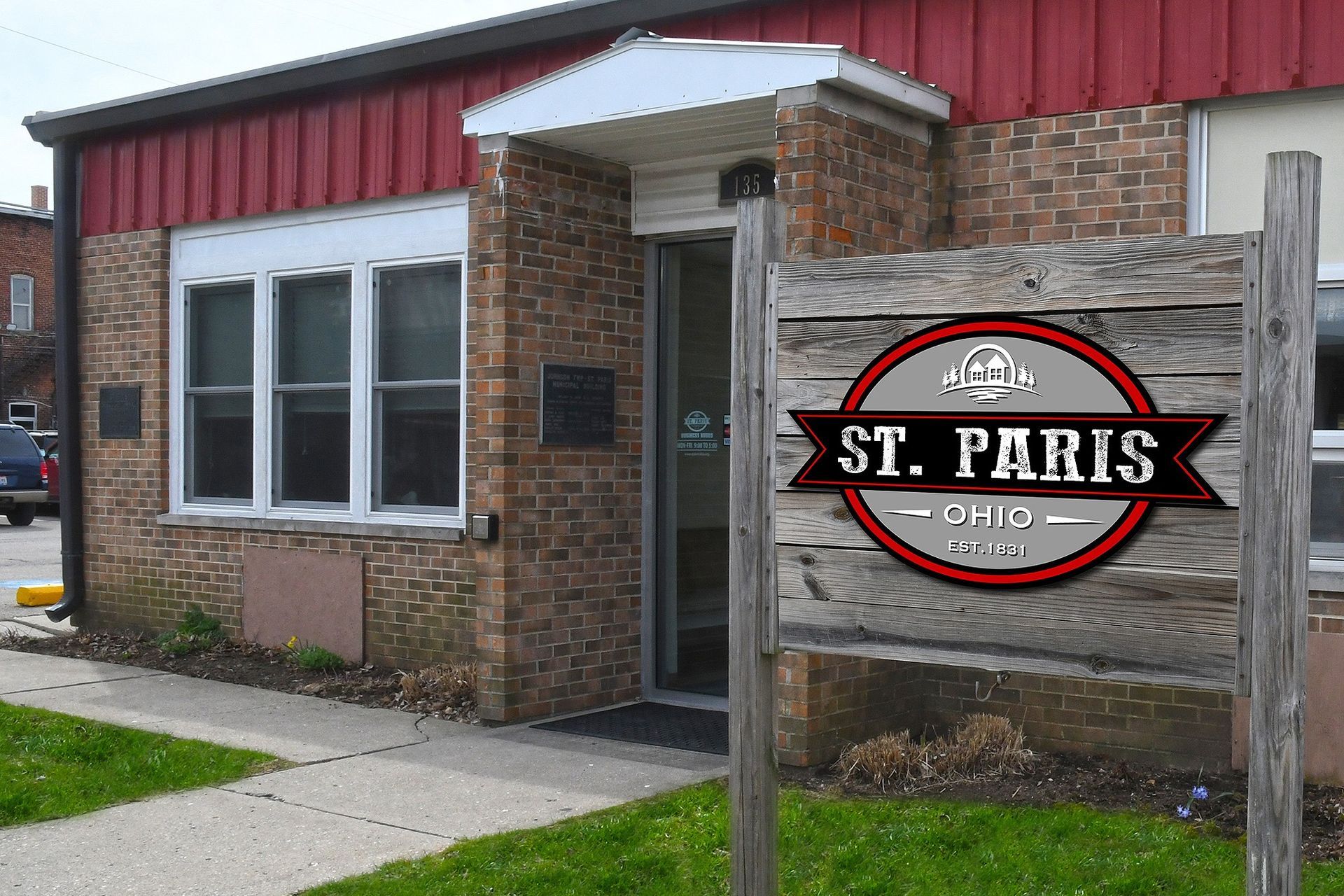 St. Paris Clinic building with a wooden sign. Brick and red facade, green grass, and sidewalk.