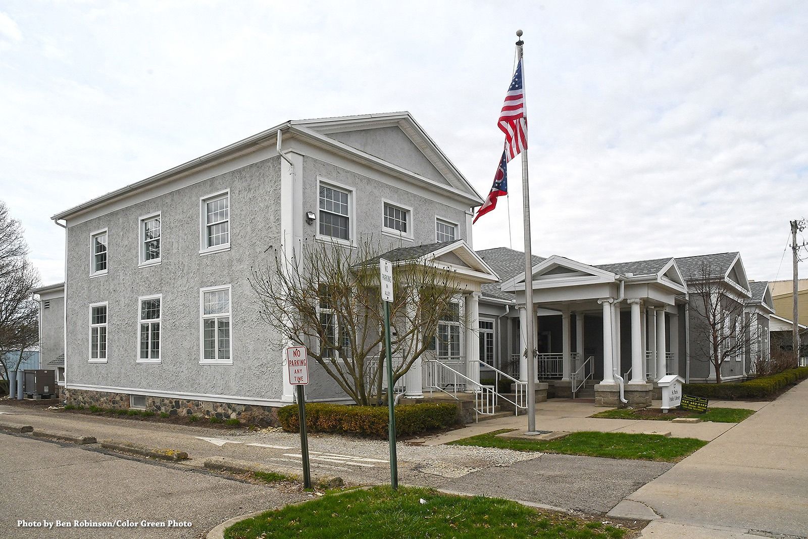 Gray, two-story building with white trim and an attached porch with columns. An American flag flies out front.