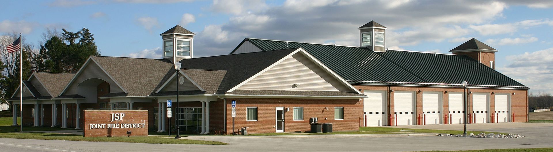 Fire station with two clock towers, red brick and white garage doors, under a cloudy sky.