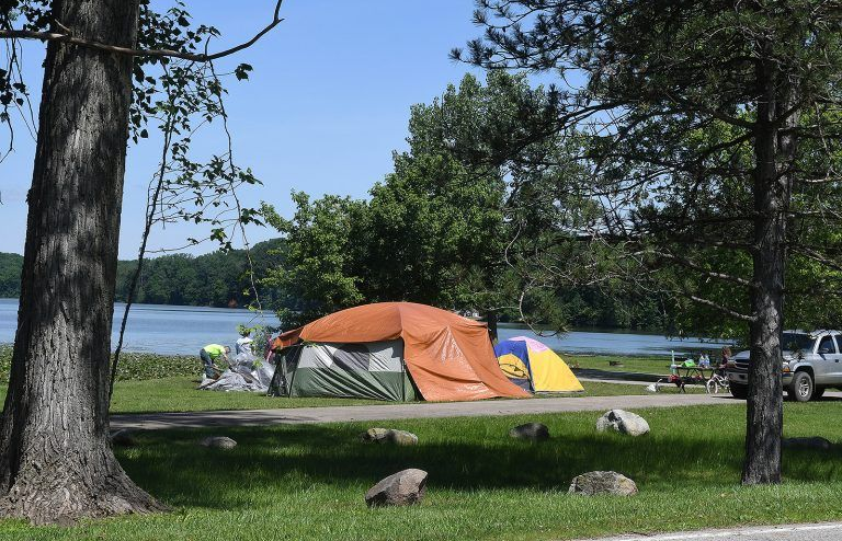 Camping tents on a grassy area next to a lake, under a bright sky.