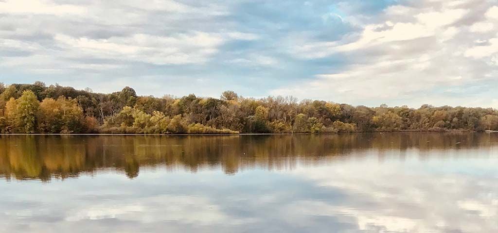 A tranquil lake reflects the cloudy sky and autumn trees on the far bank.