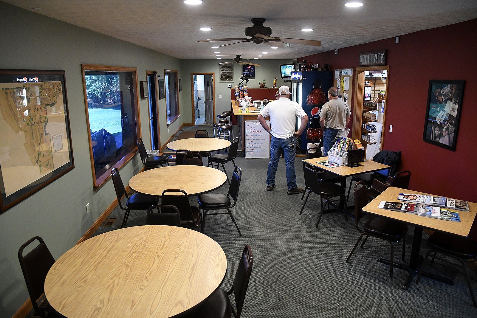Interior of a small cafe with round tables, chairs, and two men standing near a counter.