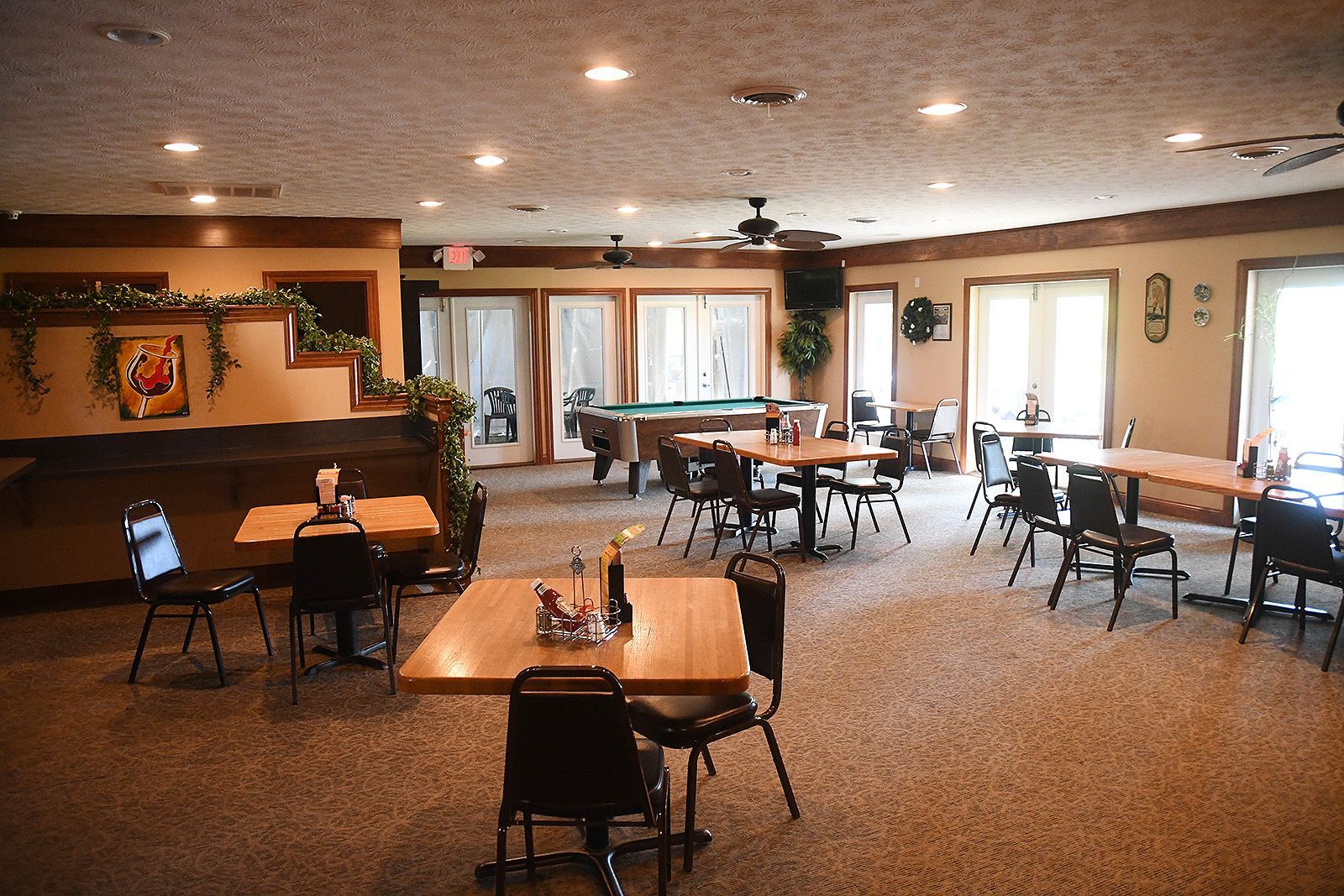 Restaurant interior with tables, chairs, a pool table, and windows.