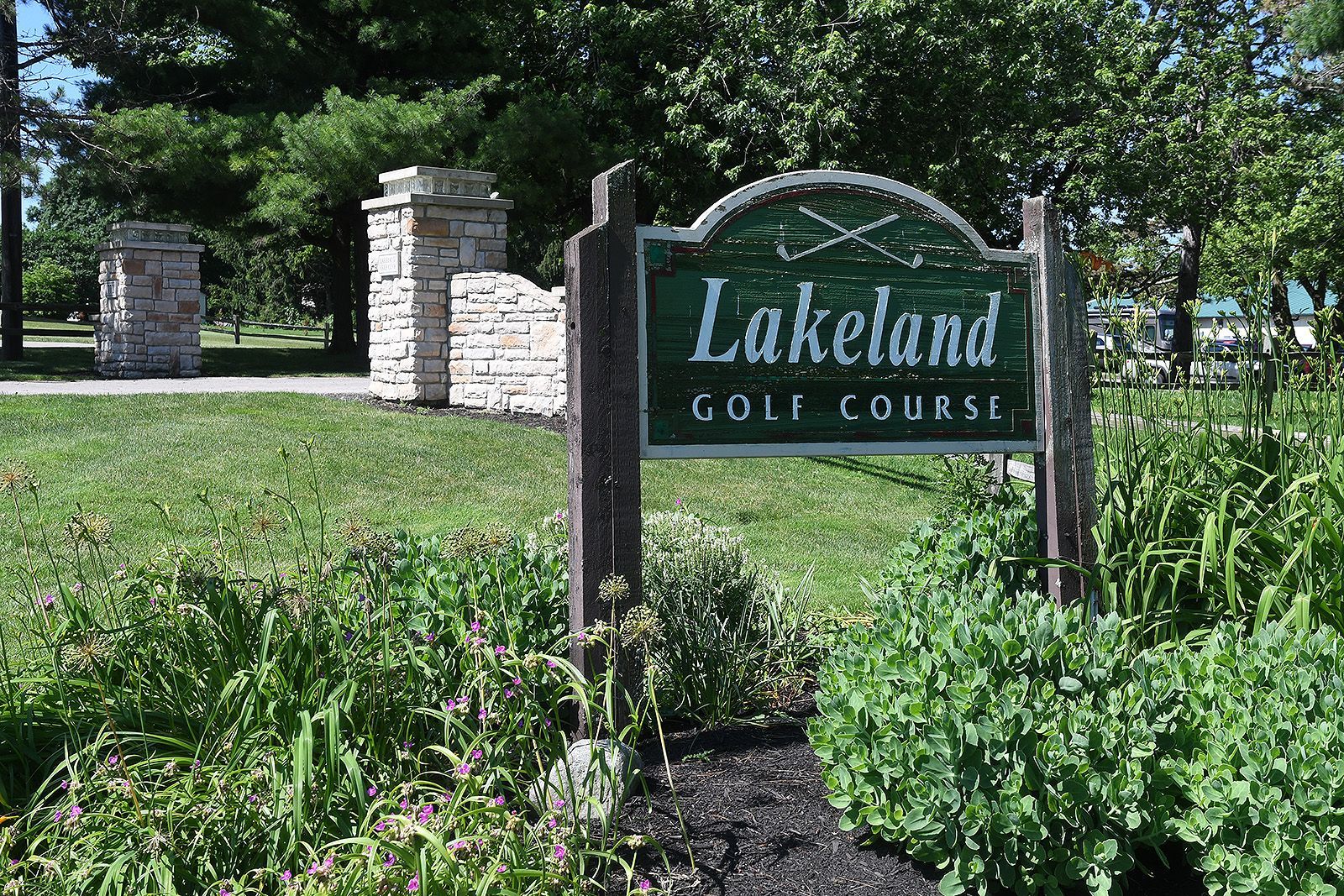 Lakeland Golf Course sign with green and white text, set in front of greenery and stone pillars.