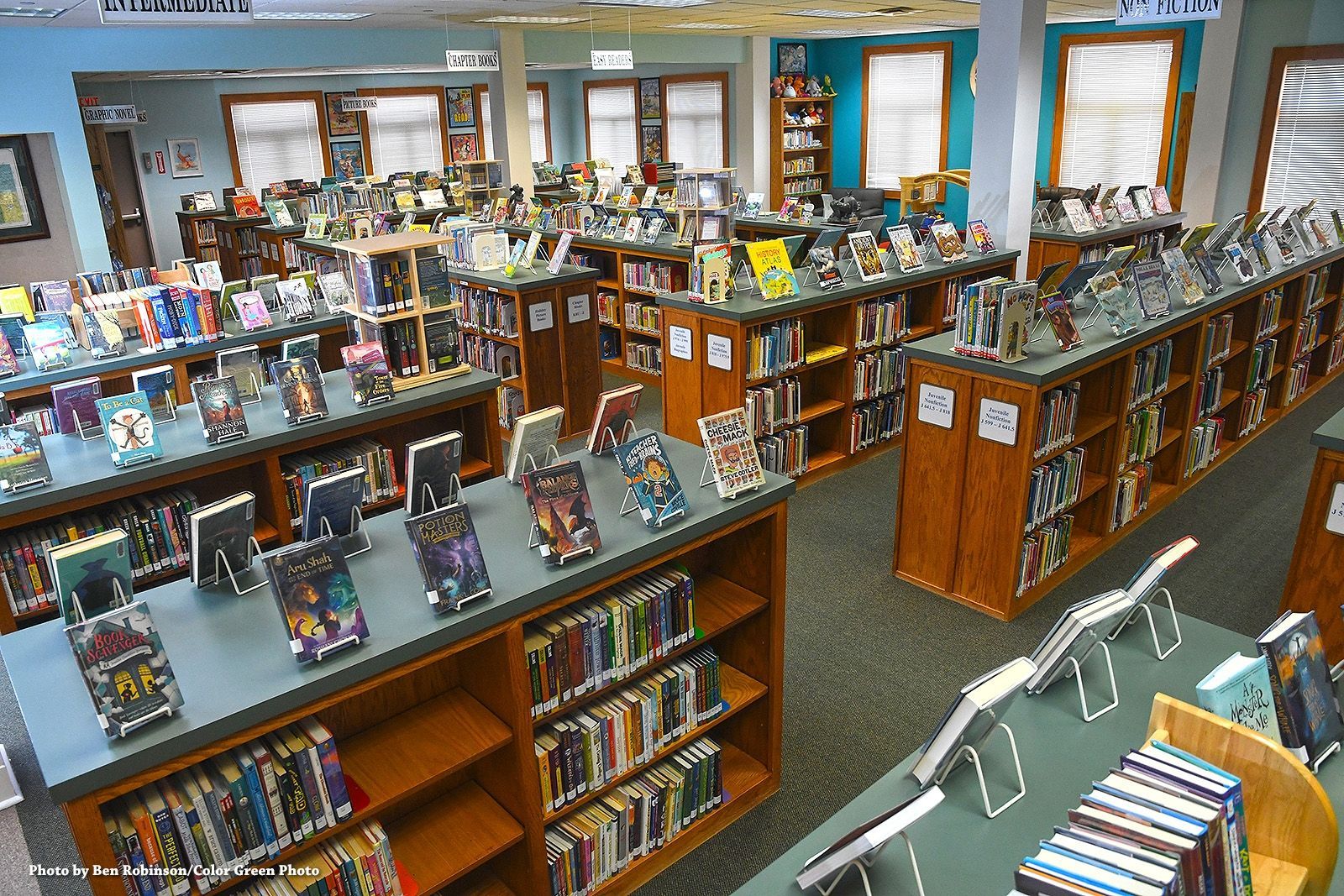 Library interior with rows of bookshelves and display tables filled with books.