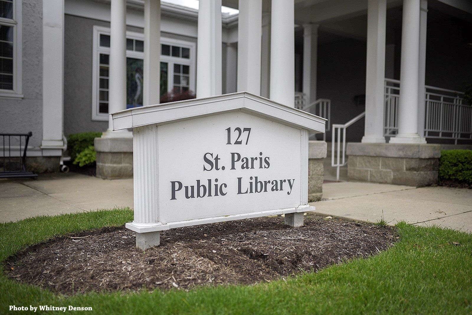 Sign for St. Paris Public Library at 127, in front of a white building with columns.