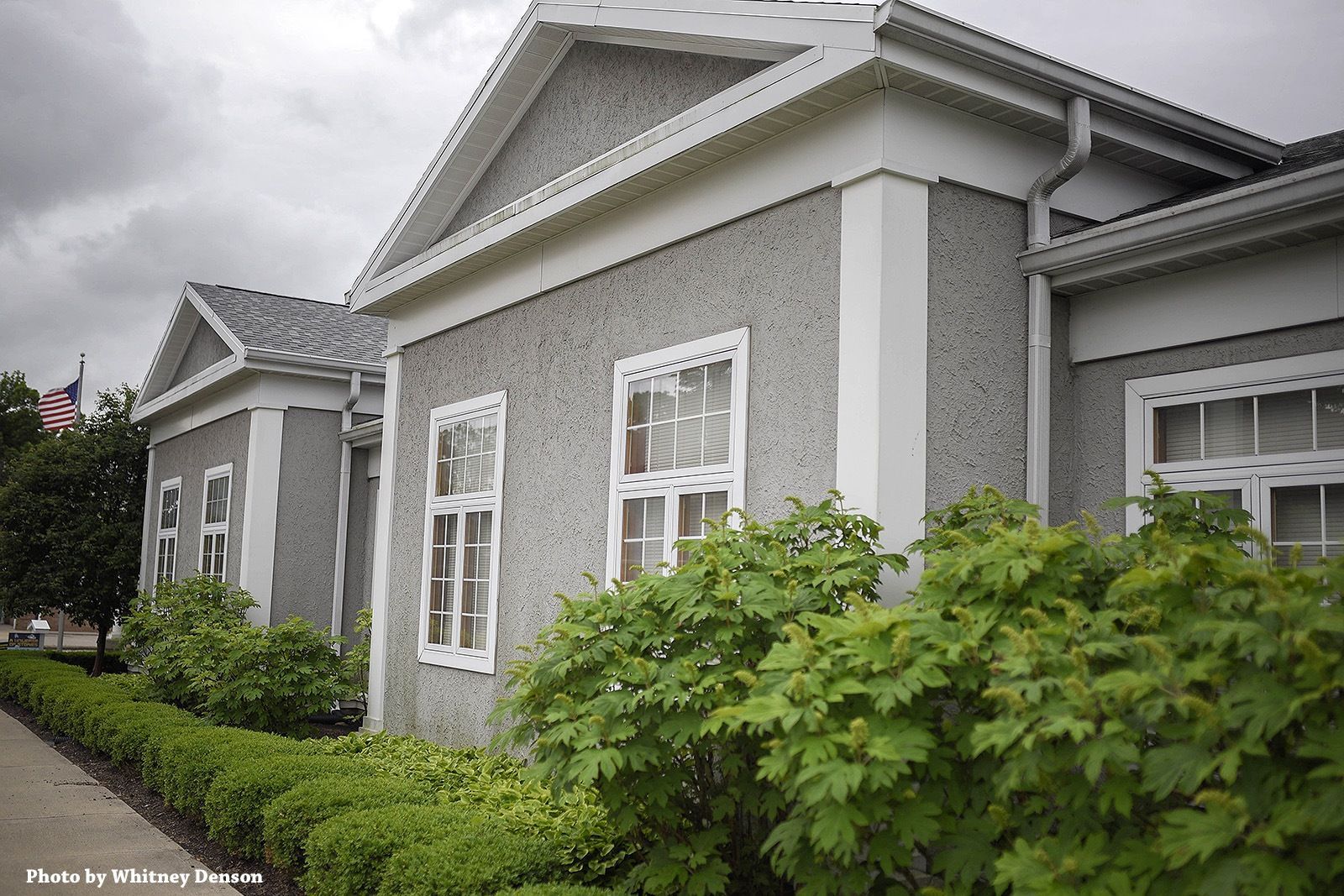 Gray building with white trim and hedges in front.