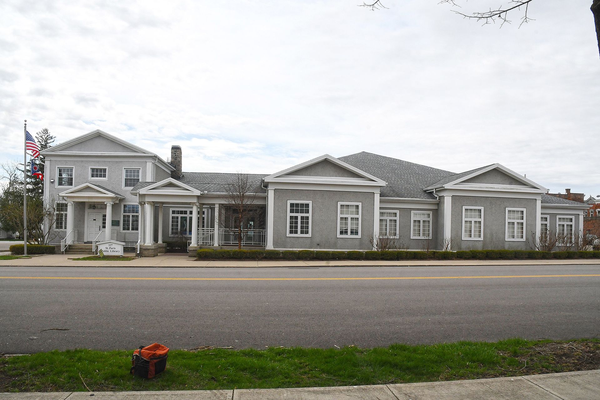 Gray building with multiple sections and white trim, beside a road.