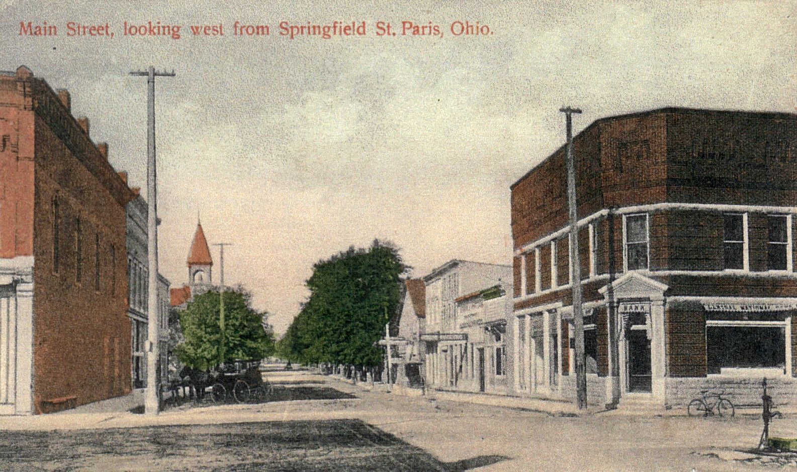 Main Street in St. Paris, Ohio, lined with brick buildings, trees, and telephone poles, circa early 1900s.