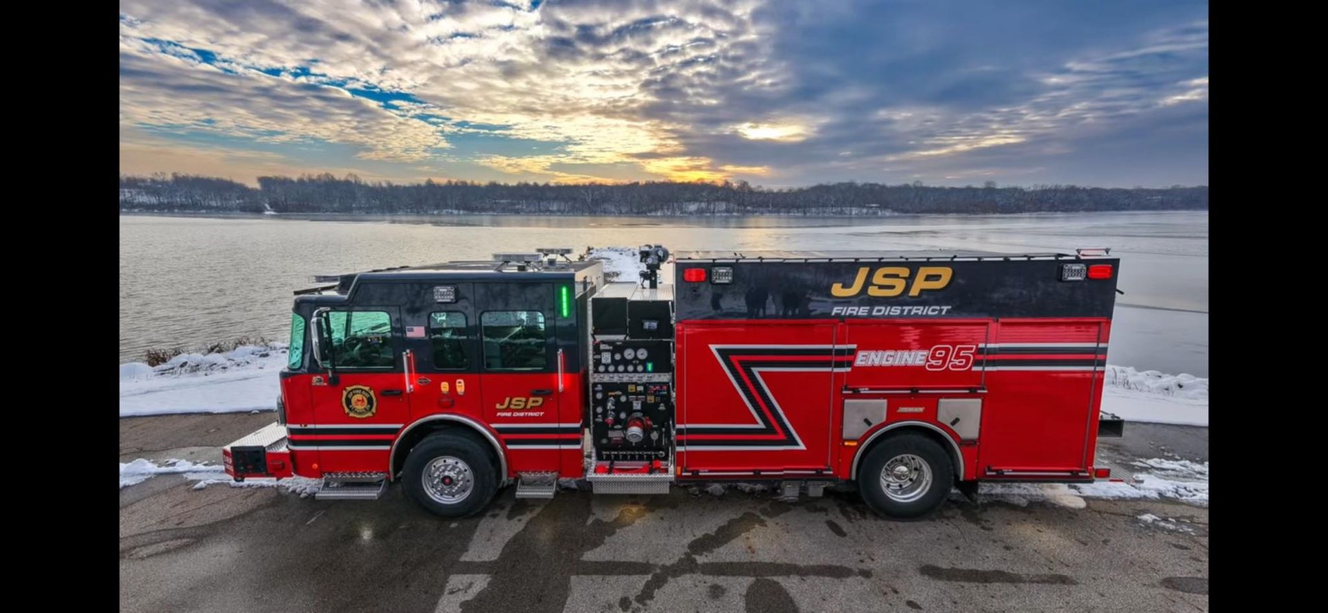 Red fire truck, JBP fire county, by a body of water under a cloudy sky.