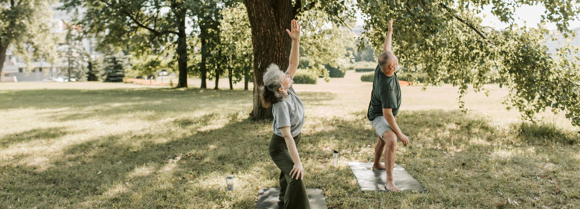 Two people doing yoga in a park, with arms raised.