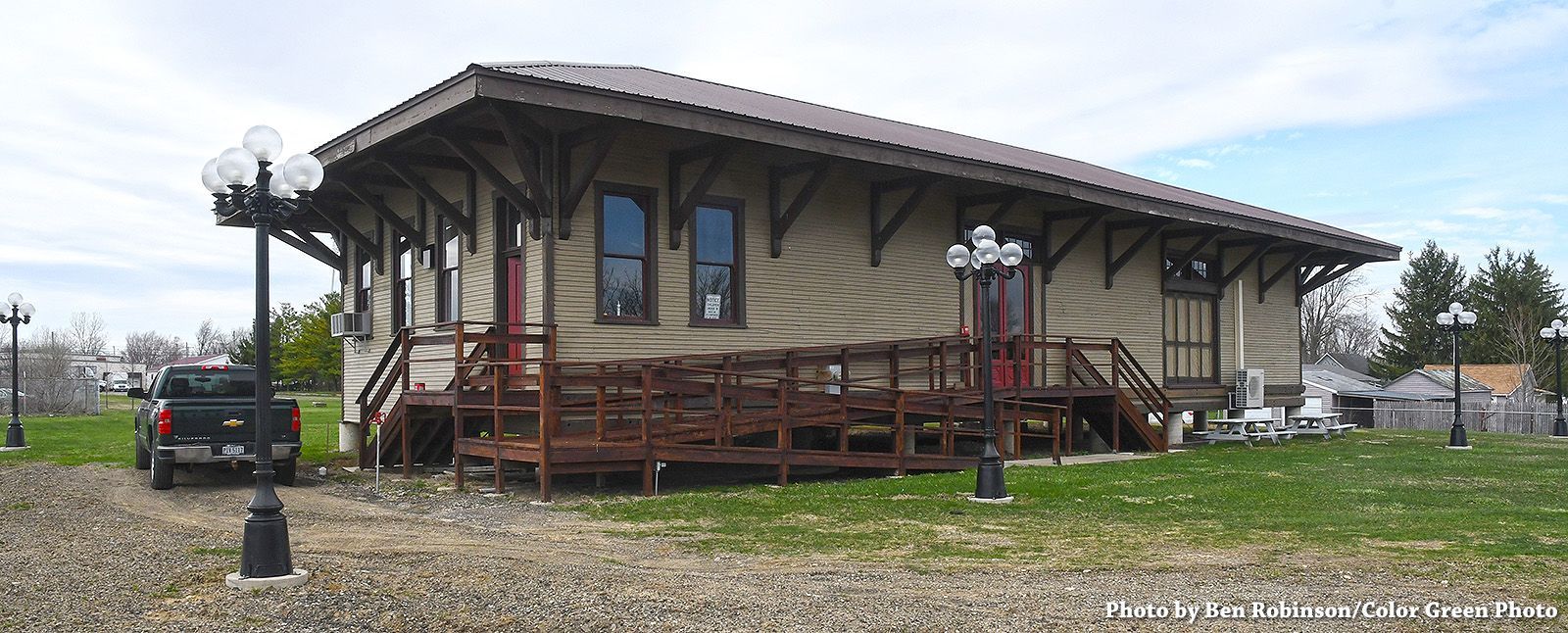 A tan-colored, old building with a brown roof and a ramp in front.
