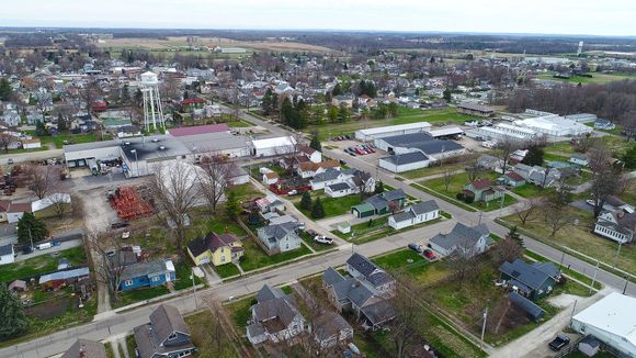 Aerial view of a small town with houses, businesses, trees, and a water tower. Overcast sky.