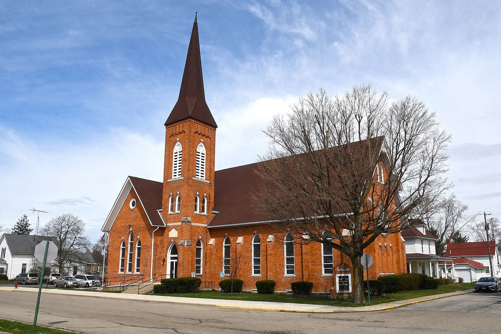 Brick church with tall steeple, brown roof, and several windows on a corner lot.