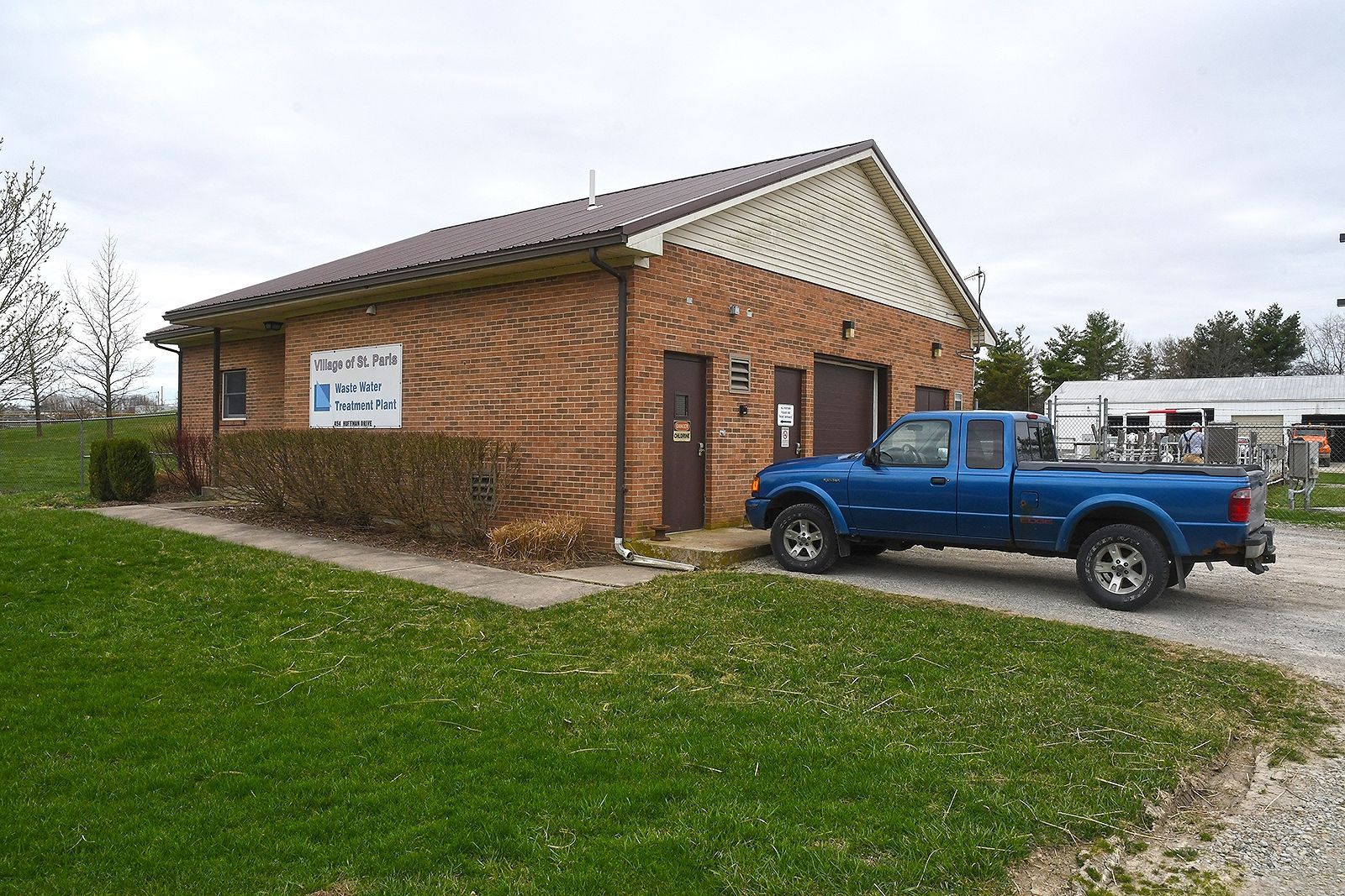 Brick building with blue truck parked out front. Sign on the side. Green grass and overcast sky.