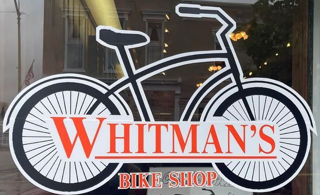 Whitman's Bike Shop logo: stylized black bicycle outline with red text on a shop window.